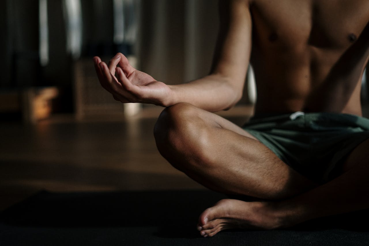 services-03 A shirtless man in a yoga studio meditating in the lotus position for relaxation and wellness.