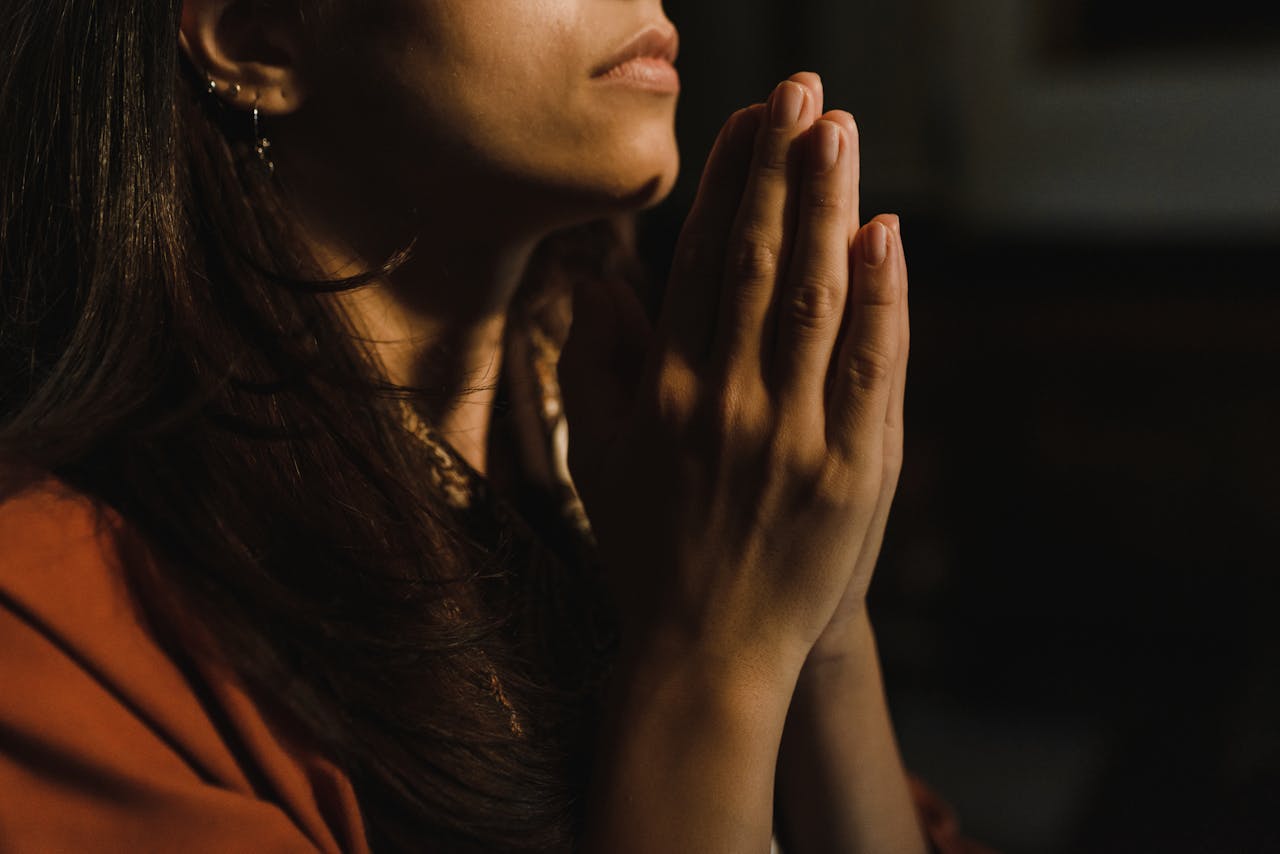 Mastering the First Impression: Your intriguing post title goes here Close-up of a woman with folded hands praying, captured in a serene indoor setting with low lighting.